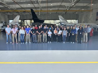 A group of students stands in front of large airplanes in a hangar.