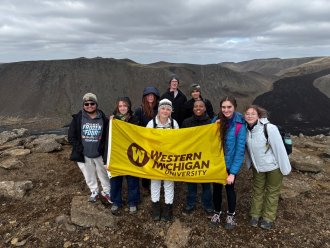 A group photo of WMU students holding a yellow WMU flag in Iceland.