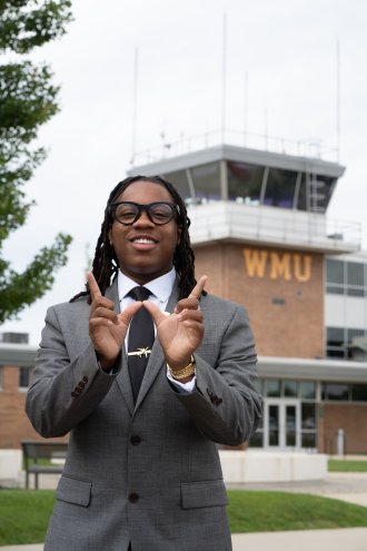 Raymond Miller holds his hands in the shape of a W in front of the College of Aviation's control tower.
