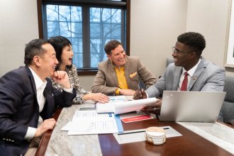Charles Zhang, Lynn Chen-Zhang, President Russ Kavalhuna and Mo Tall sit around a conference room table.