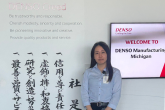 Momoka Ichikawa stands next to Japanese letters and a sign for Denso.