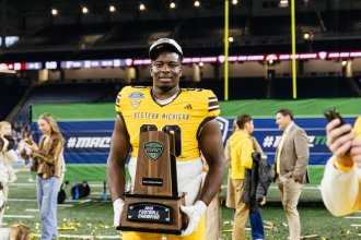 WMU football player smiles while holding the MAC trophy.