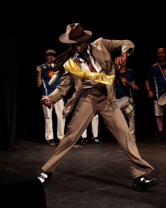 A man wearing a period hat and suit dances on a dance floor.