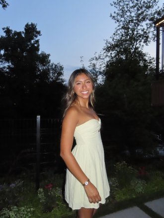 Joslyn Figueroa is wearing a white strapless dress, standing outside in the evening, smiling. 