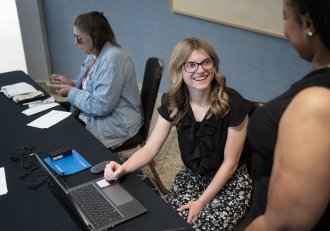 Mackenzie Flood sits at a table while talking to a colleague.