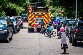 Kids ride bikes behind a firetruck.