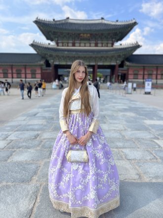 WMU study abroad student studies abroad in Korea. She is wearing traditional clothing and standing in front of an old Korean building. 
