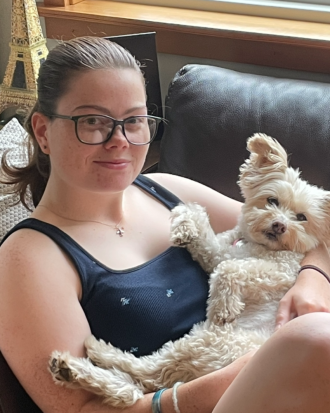 Amanda Gowey sits with her cute little dog in her lap, smiling.