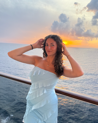 Avery Perleberg, wearing a light blue strapless dress, smiles on the deck of a boat at sunset.