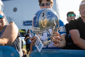 A Detroit Lions fan stands on the practice sideline holding an autographed helmet.