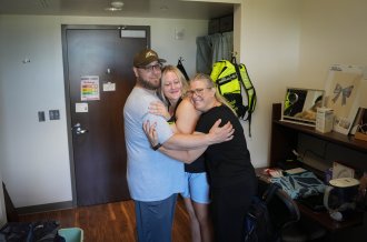A family hugs in a dorm room.