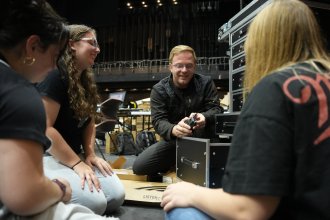 Instructor Josh Reid kneels on the floor and talks to students.