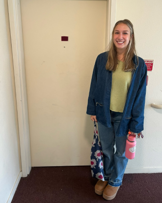 Elsa Marotzke Stands outside an apartment door with water bottle and tote, smiling. 