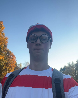 Tyler Kitchen is dressed like "Where's Waldo?" wearing a white and red striped shirt and beanie, and black, round framed glasses.