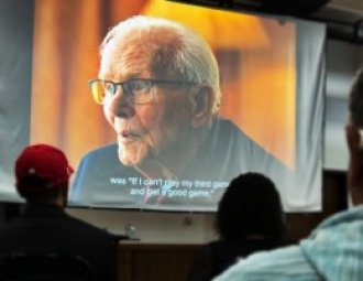 Audience looking at movie screen projecting older man from documentary film