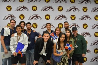 Students wave the flags of their home countries in front of a Bronco backdrop at International Student Orientation.