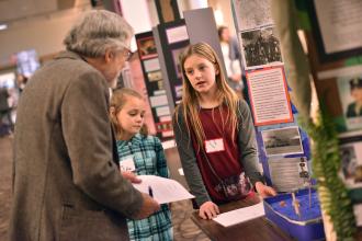 Two female students explain their display to a judge