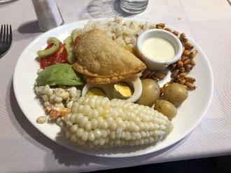 A plate of local food including corn, potato, avacado and chicken in a restaurant.