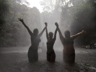 Three girls swimming in a waterfall under the rain.