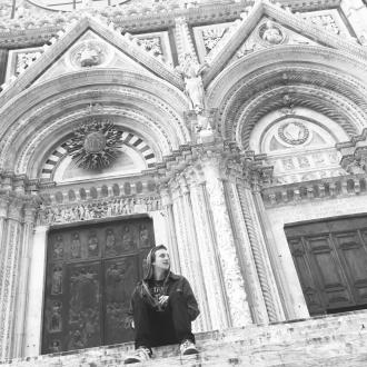 A boy sitting on the stairs in front of an old building in Italy, wearing hoodies.