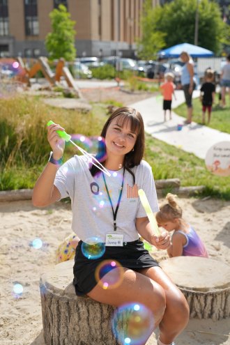 Jenna Robinson blows bubbles through a large wand outside.