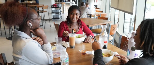 Three students sit at a table in a restaurant eating raman and drinking boba tea.