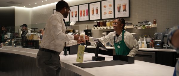 A student Starbucks employee hands a customer their coffee over the counter.