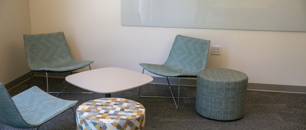 Three chairs and two short stools sit around a small white table in the corner of a Valley Oaks study lounge.