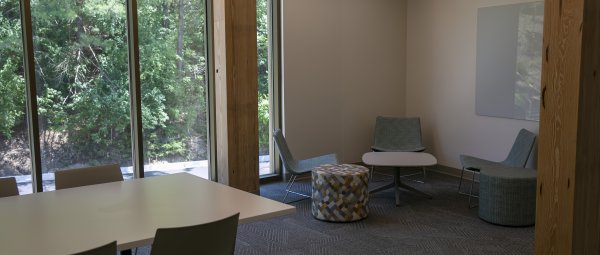 A multipurpose lounge featuring study tables, a whiteboard, wood columns and large floor to ceiling windows.