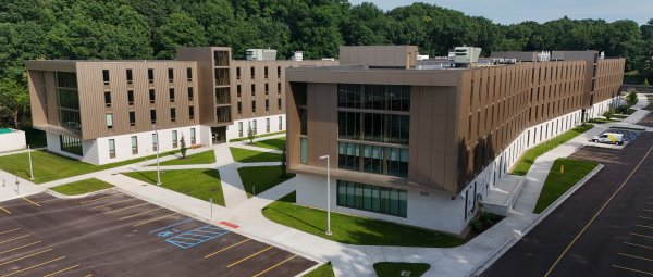 A drone shot of a modern, H-shaped residence hall with a brown exterior, large windows, and a courtyard with sidewalks cutting through it.