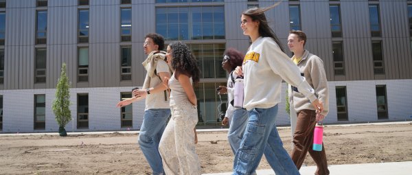 A group of Western students wearing WMU branded clothing walk on a sidewalk in the Valley Oaks courtyard. 
