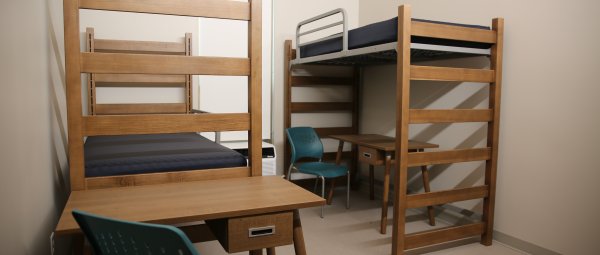 An undecorated Valley Oaks residence hall room with two lofted beds, two desks, and two teal desk chairs.
