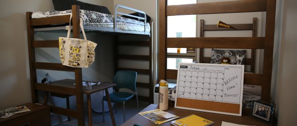 A decorated residence hall room with two lofted beds on either side of a tall window.