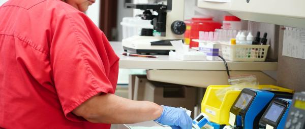 Medical Assistant manages testing of samples at table, with test machines