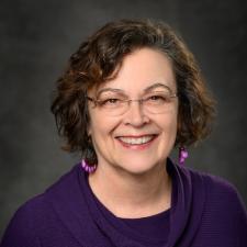 Professional photo of Andrea Allen wearing a purple sweater in front of a grey background