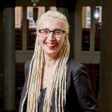 N. Kıvılcım Yavuz, a smiling white person with long blond dreadlocks, poses for a portrait.