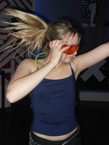 Woman with colored sunglasses on, dancing with her hair flying behind her.