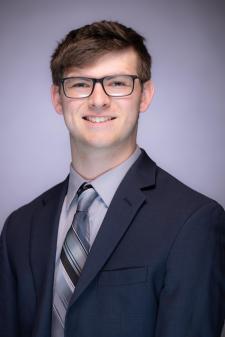 Headshot of Kevin Wirght in a black suit with a grey stiped tie on a grey background