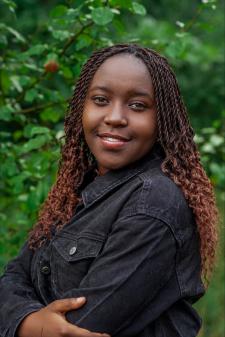 Headshot of Hosanna Ndikumana in a black jacket with greenery in the background