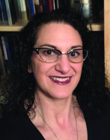 Woman with dark curly hair, wearing glasses and smiling.