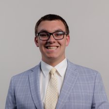 Headshot of Landon Wiedenhoeft in a grey suit with yellow tie on a white background.