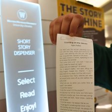 A student holds up a printed story from the Story Machine in Waldo Library.