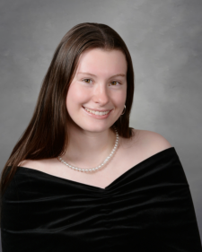 Headshot of Maddie Suttle in a black top on a grey background.