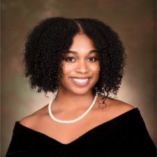 professional photo of Jaylin Nesbitt in a black top with a pearl necklace in front of a tan background