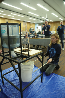 Science Olympiad contestant participating in an event where water flows into a bucket through pipes