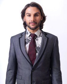 Performer Gabby Galore out of drag makeup, wearing a gray suit and red tie