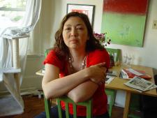 A woman sitting backwards on a chair, wearing a red shirt with her arms crossed. 